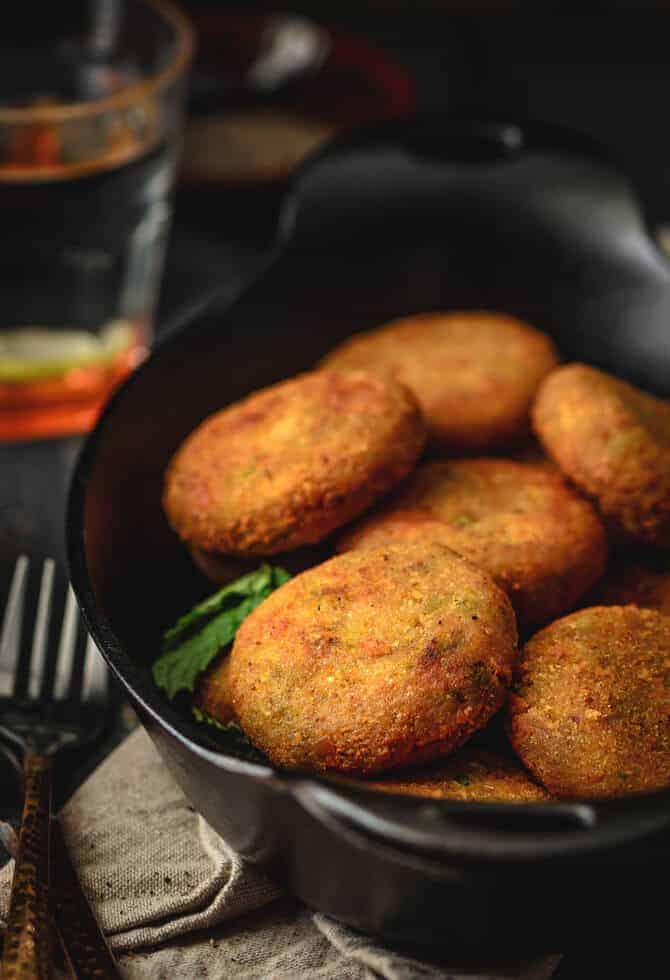 Paneer cutlets served in a black bowl. The bowl is placed on a diner table and the picture is clicked from top-front angle.
